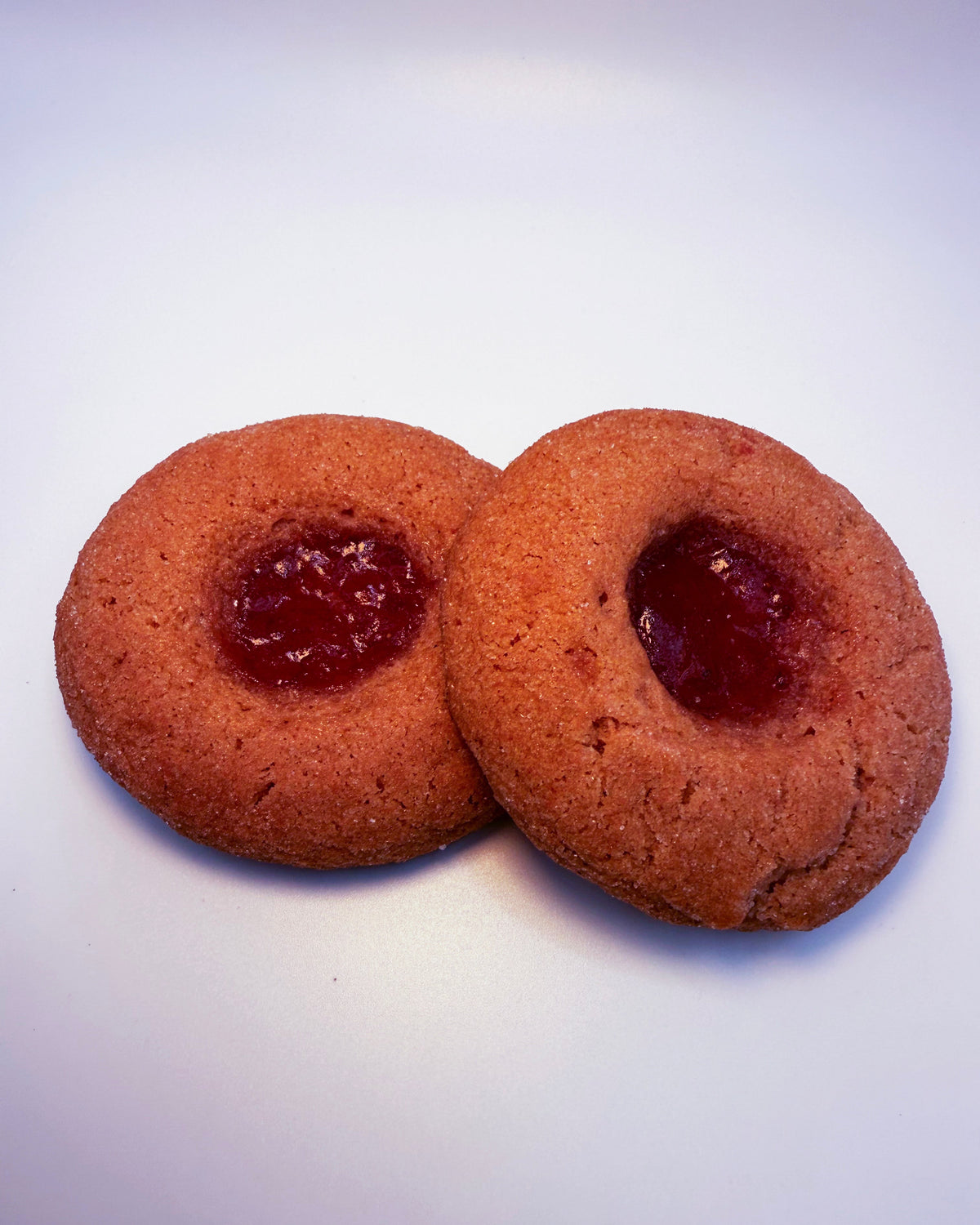 Two strawberry cookies with jelly filling on a white background
