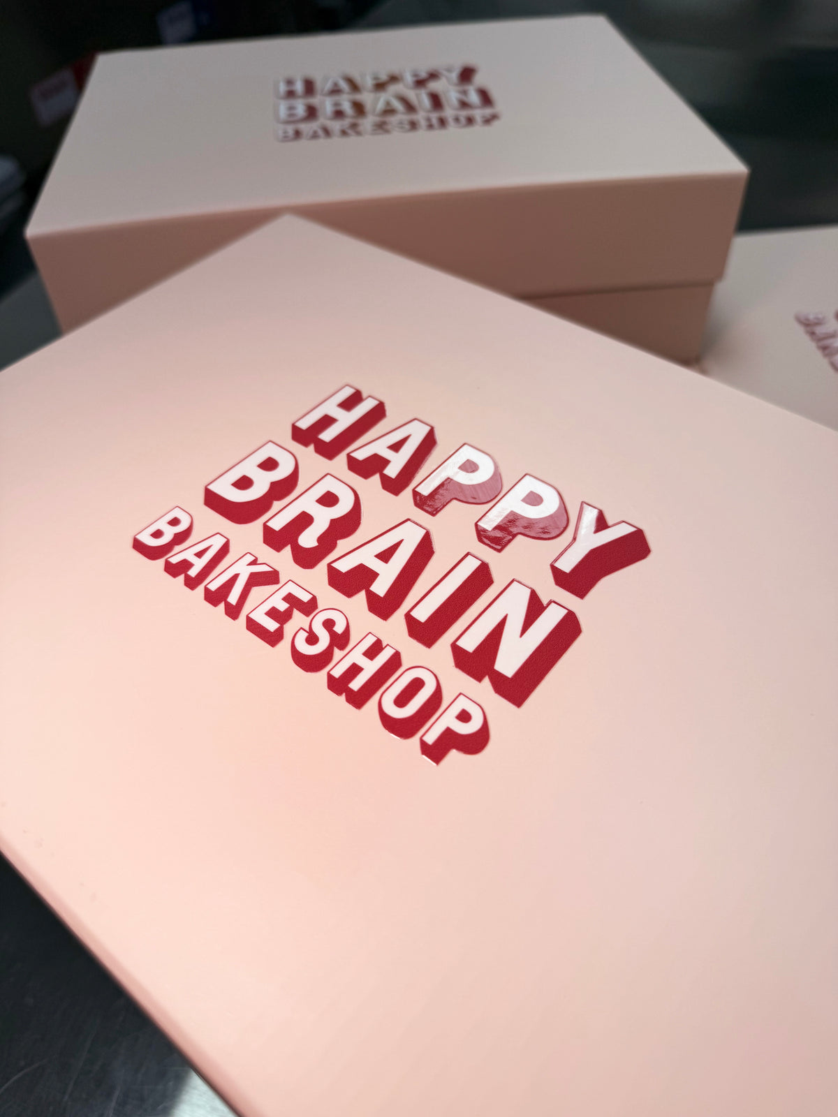 Pink packaging with 'Happy Brain Bakeshop' branding on a dark background