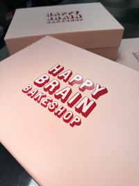 Pink packaging with 'Happy Brain Bakeshop' branding on a dark background