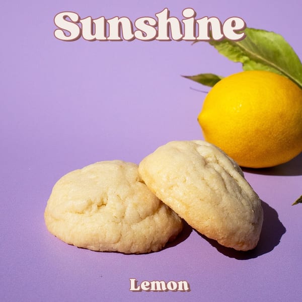 Two lemon cookies on a purple background with a whole lemon and green leaves.