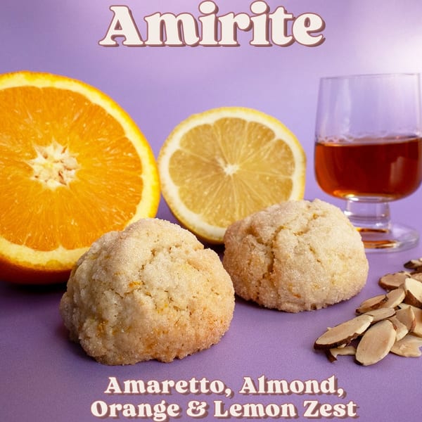Two Amaretto cookies with orange and lemon halves, sliced almonds, and a glass of amber liquid.