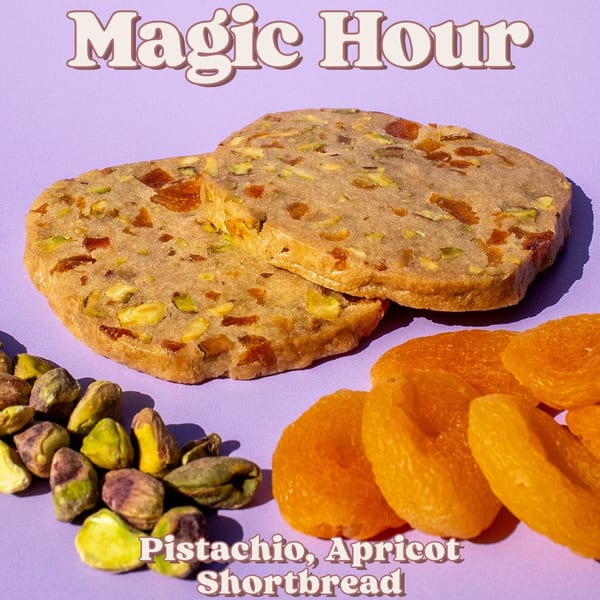 Two pistachio and apricot shortbread cookies with loose pistachios and dried apricots on a purple background.