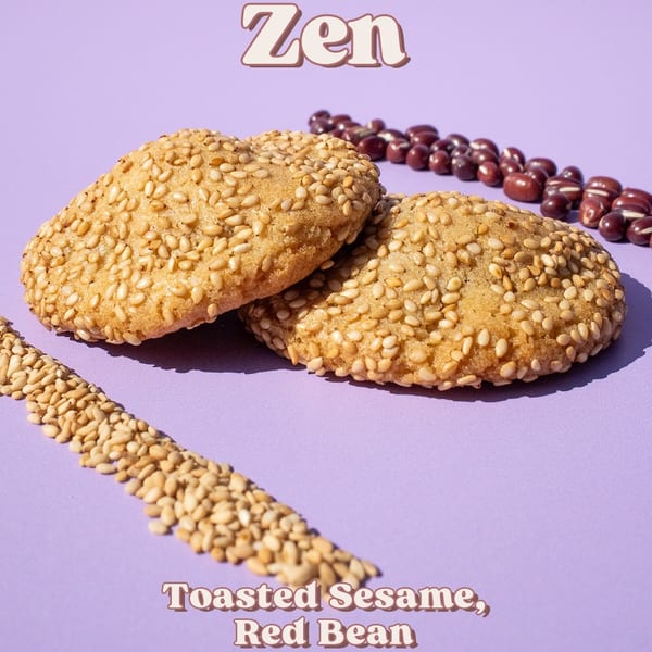 Two sesame cookies with red beans and loose sesame seeds on a purple background.