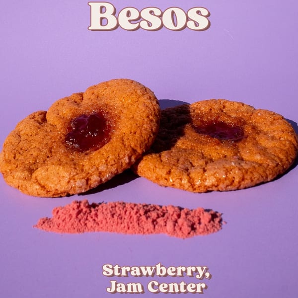 Two Besos strawberry jam center cookies with strawberry powder on a purple background.