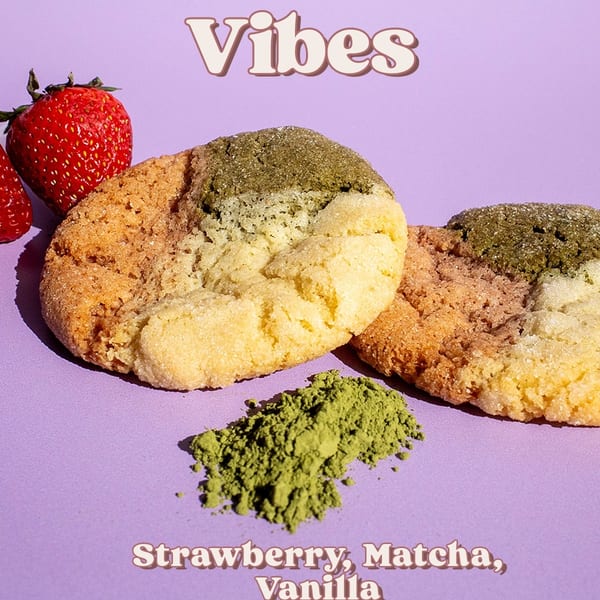 Two tri-color cookies with strawberries and matcha powder on a purple background.